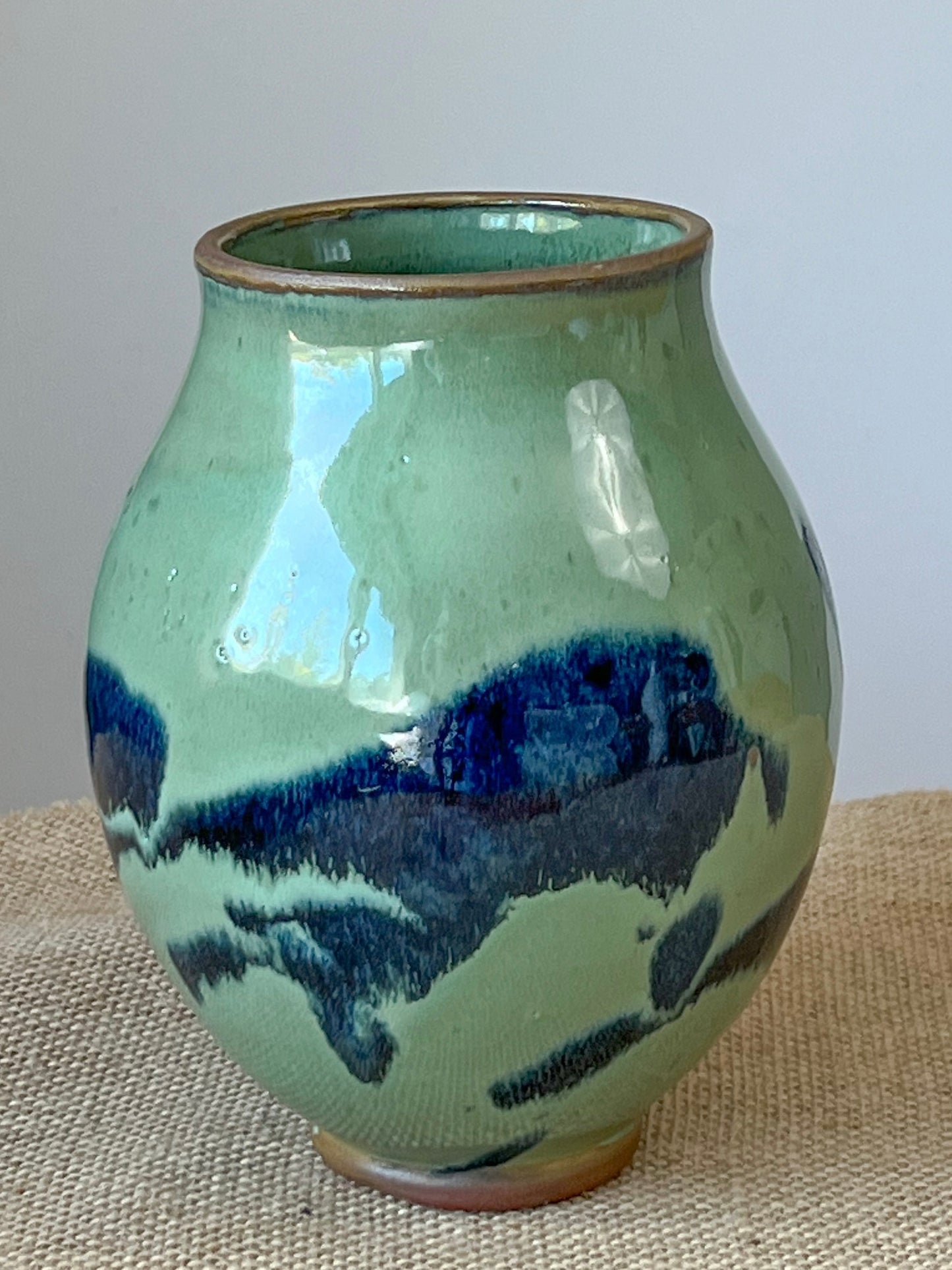 Wheel thrown vase using a red stoneware clay. Splashes of blue play across the algae green surface.