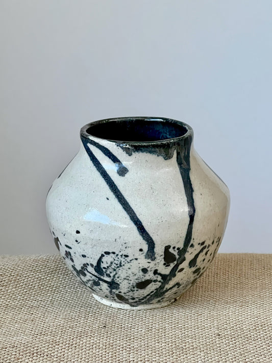 Wheel thrown vase with stoneware clay. Black glaze was dripped and flicked over the white vase. Interior finished in black.