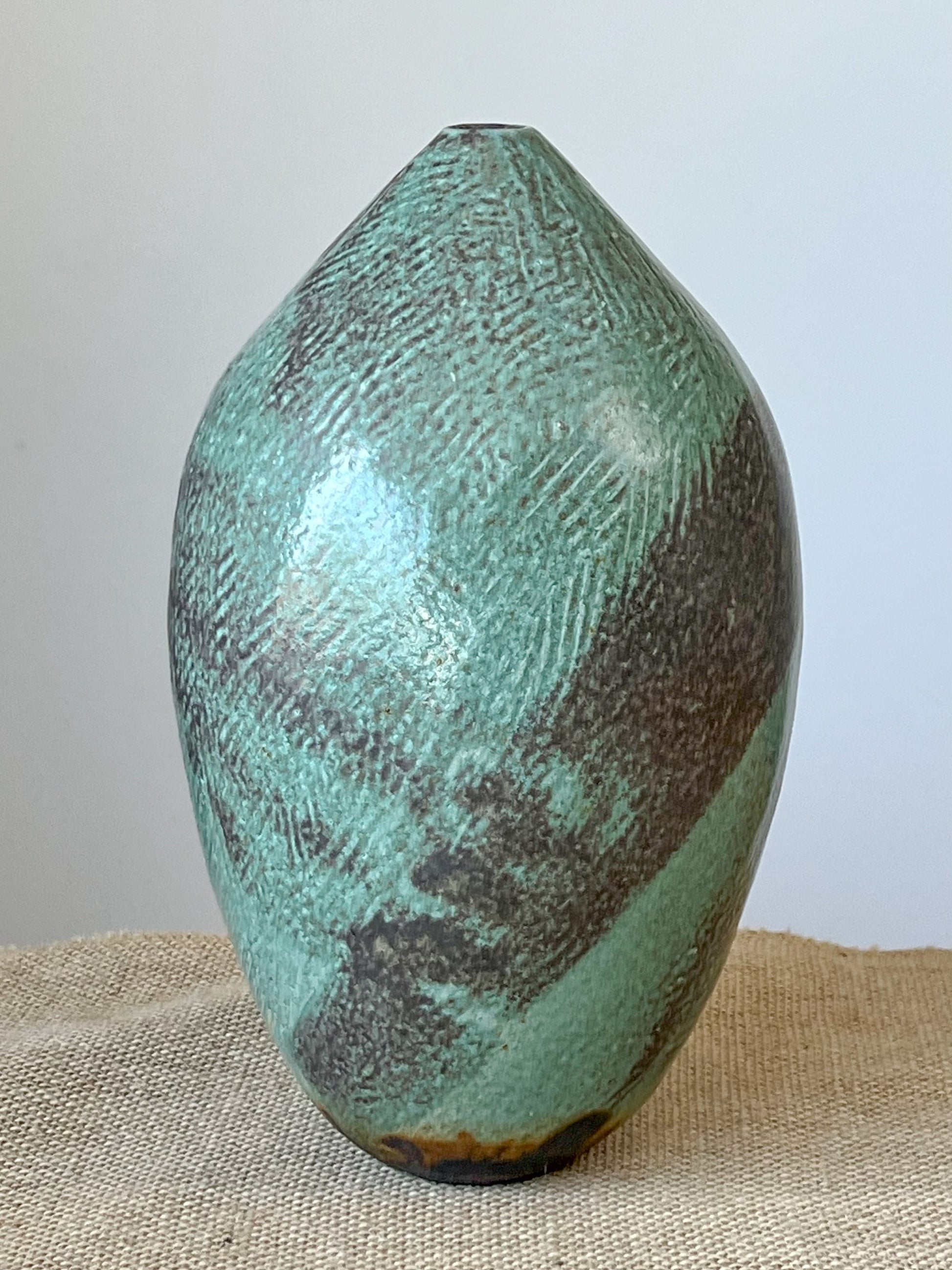 Wheel thrown vase using stoneware clay. Vase was hand carved with texture, covered with an iron oxide and then a jade/blue glaze was poured on.