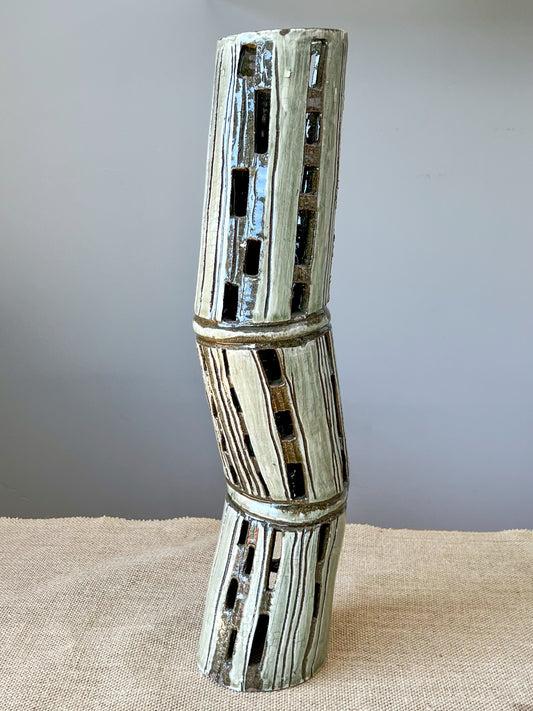 Wheel thrown dark brown form using stoneware clay. The dark brown clay forms were altered, colored with a white slip and carved. A green celadon glaze covers the luminary.