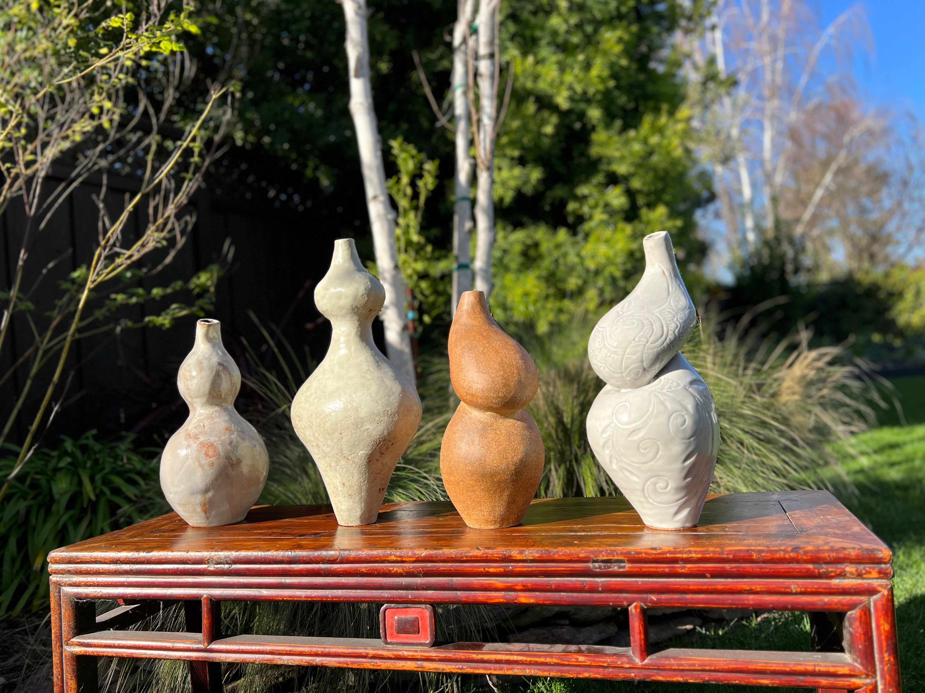 Four hand carved curved clay sculptures, titled Vessels. Finished with white glaze or left bare.
