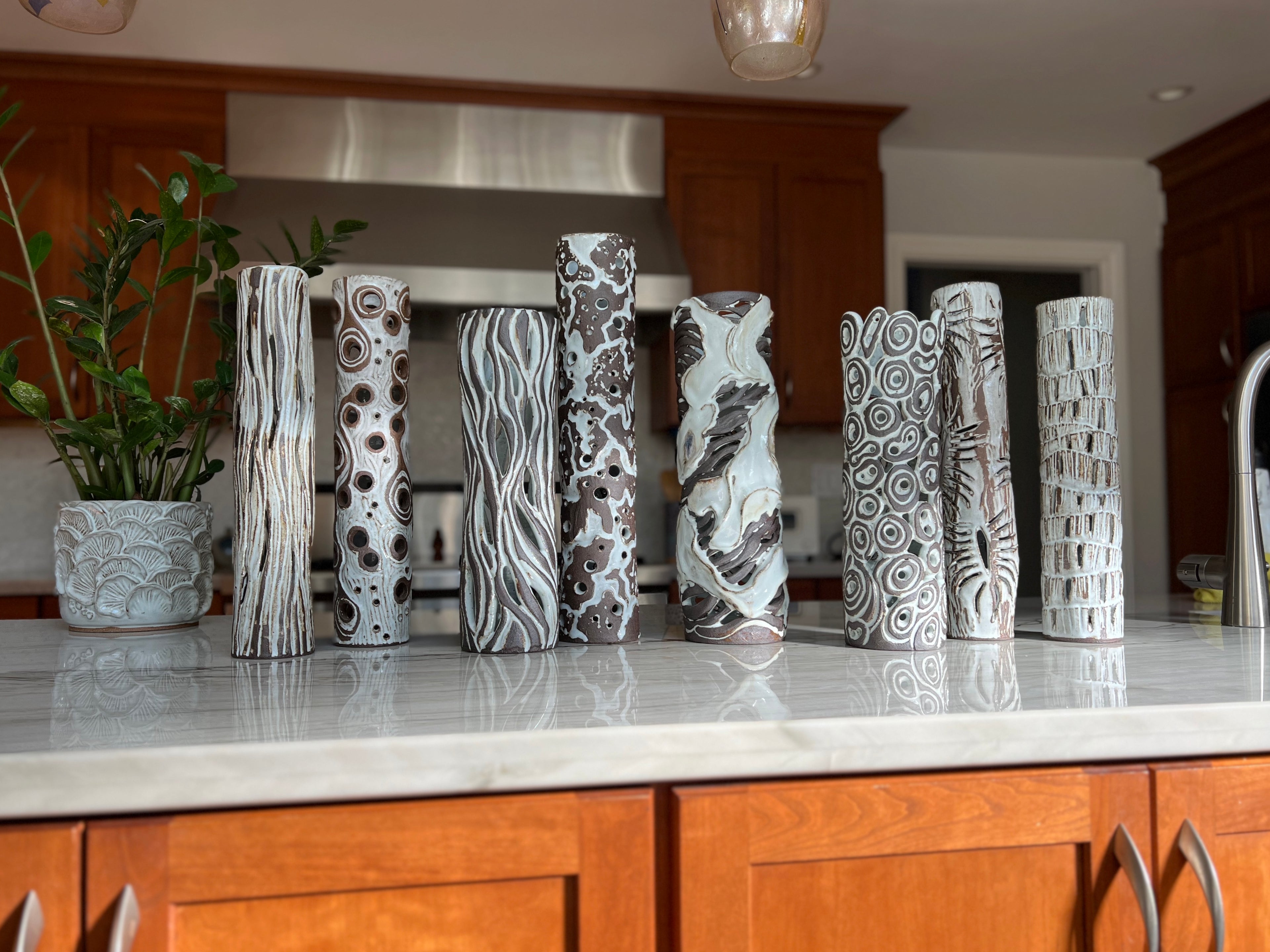 A series of tall white and dark brown luminaries. Hand thrown and hand carved clay sculptures.