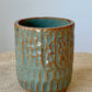Wheel thrown cylinder using brown stoneware clay. Top rim is altered to an oval. Hand carved texture is highlighted with the blue green glaze.