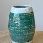 Wheel thrown vase using stoneware clay. The band of green glaze highlights the carved lines. A white glaze finishes the piece.