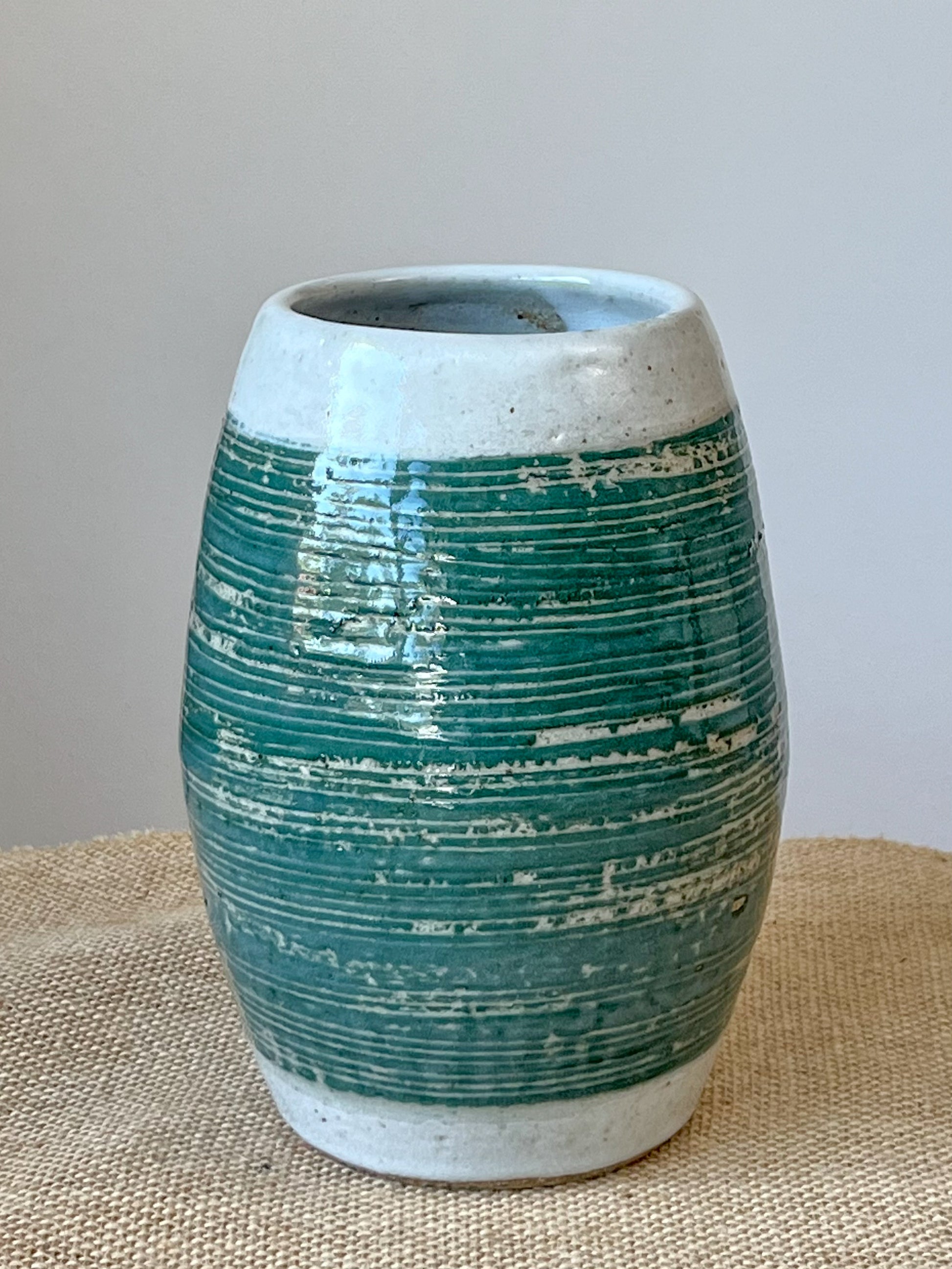 Wheel thrown vase using stoneware clay. The band of green glaze highlights the carved lines. A white glaze finishes the piece.