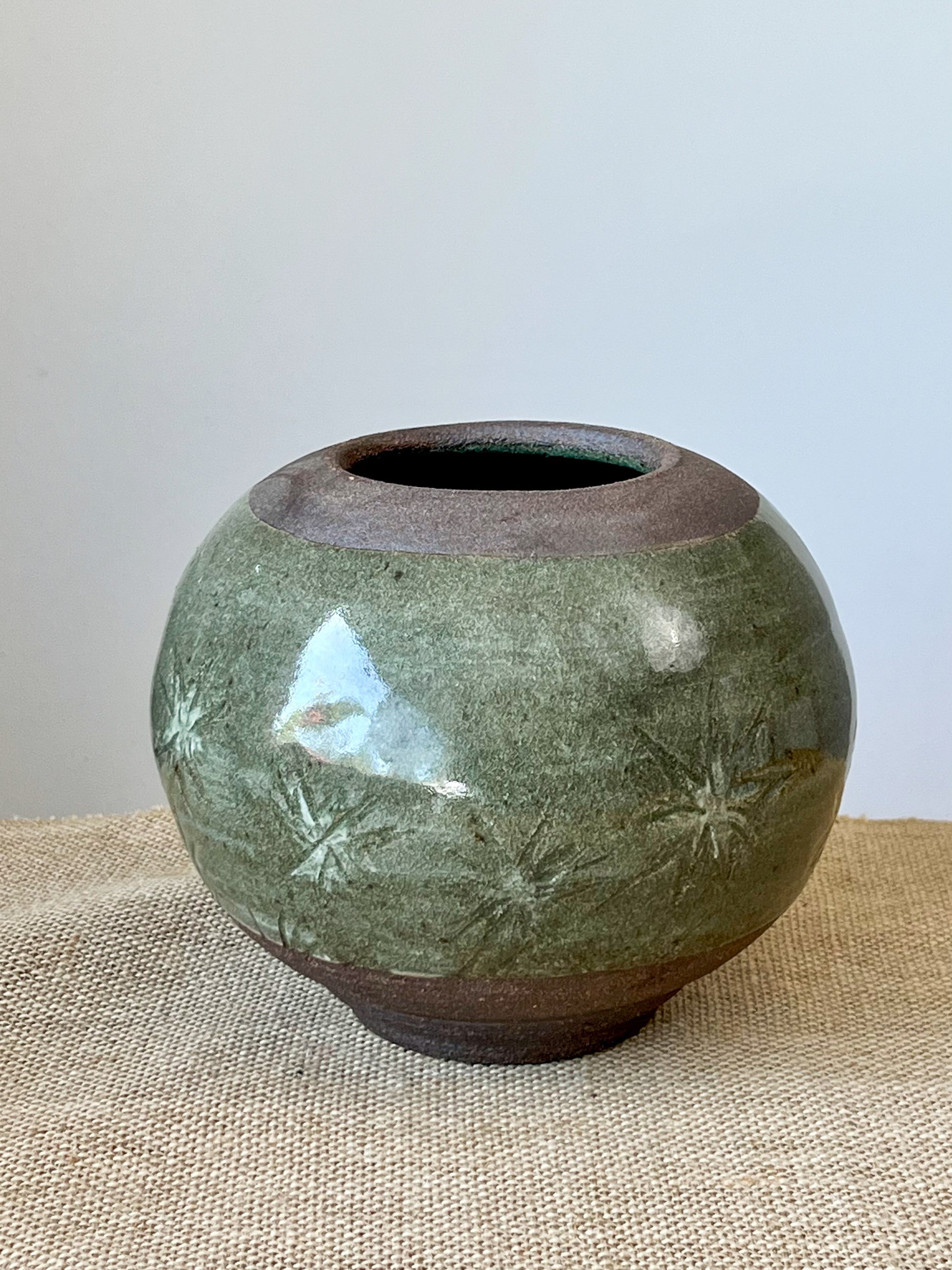 Wheel thrown stoneware clay. A band of green covers the belly of the dark brown clay. Hand carved.