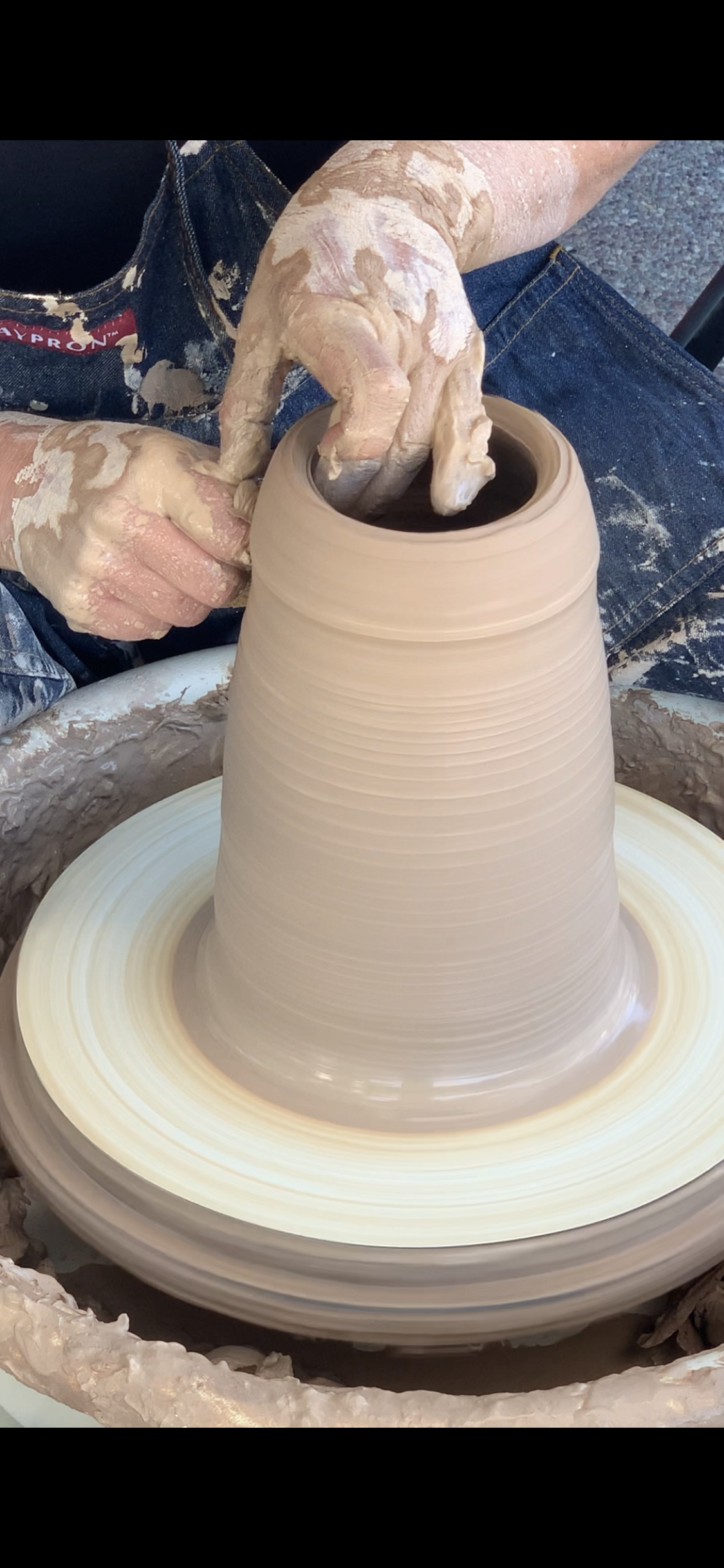 A potter throwing a clay pot on the wheel. Two hands are pulling the pot taller.